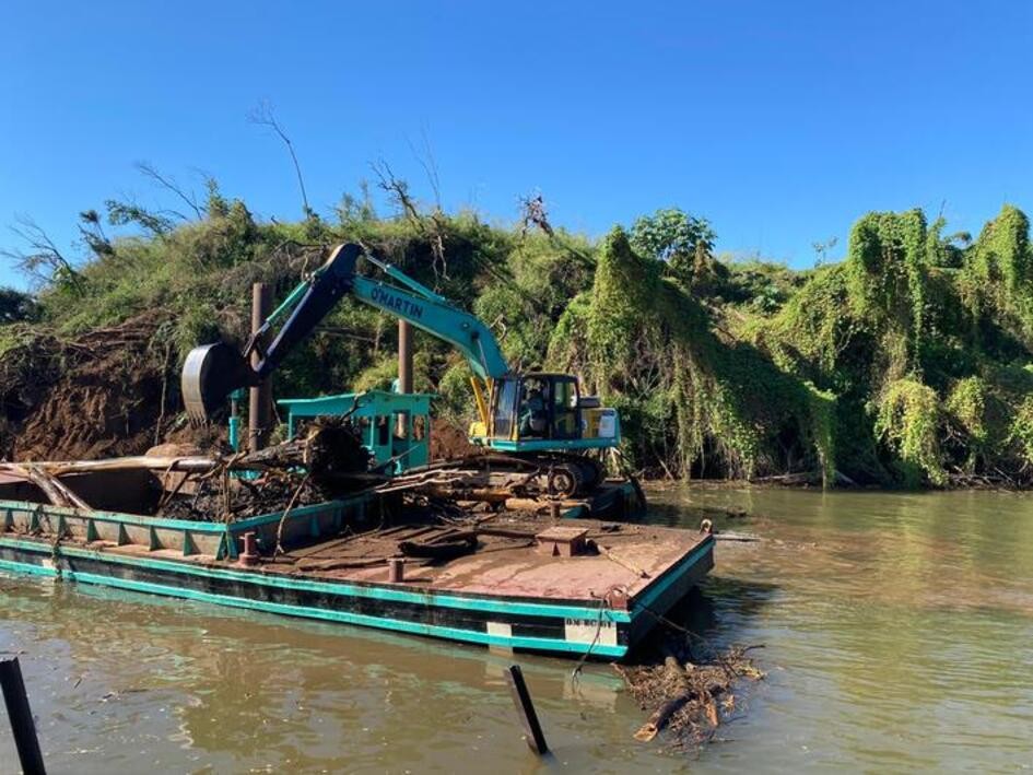 Escavadeira hidráulica instalada sobre uma balsa metálica, realizando serviços de limpeza e dragagem