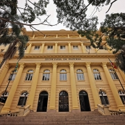 Foto frontal, levemente de baixo para cima, da fachada da Sefaz. O prédio é amarelo, em estilo neoclássico, e no centro se lê "Secretaria da Fazenda" em letras negras. Ao lado, há palmeiras. No inferior da foto, aparece parte da escadaria que leva ao edifício.