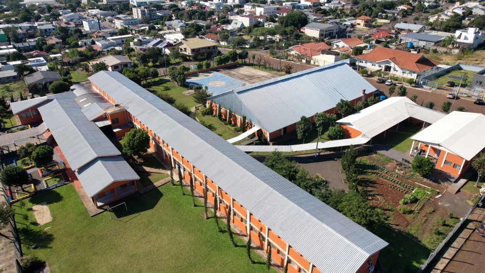 Foto aérea da escola, que é composta por quatro edifícios horizontalizados de cor alaranjada e telhados cinza. Ao redor, aparece parte da cidade.