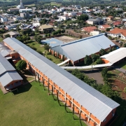 Foto aérea da escola, que é composta por quatro edifícios horizontalizados de cor alaranjada e telhados cinza. Ao redor, aparece parte da cidade.