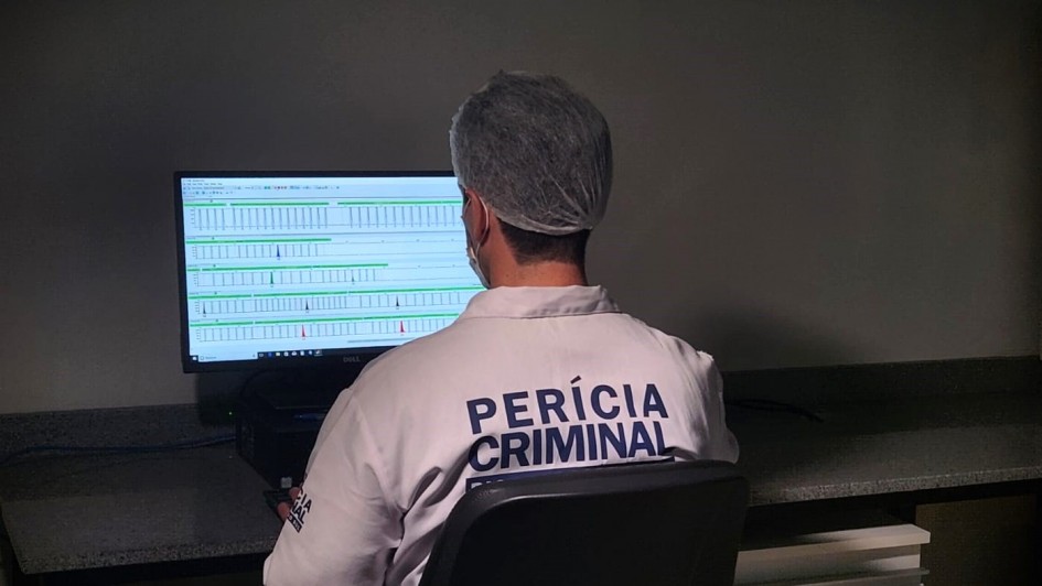 Imagem mostra um homem de costas, olhando para um computador. Nas costas, a roupa estampa a seguinte inscrição "Perícia Criminal".