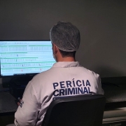 Imagem mostra um homem de costas, olhando para um computador. Nas costas, a roupa estampa a seguinte inscrição "Perícia Criminal". 