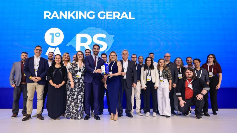 A imagem mostra um grupo de cerca de 20 pessoas reunidas, sorrindo e posando para a câmera. Ao centro, está o governador Eduardo Leite e a titular da SPGG, Danielle Calazans, segurando um troféu. No painel ao fundo, pode-se ler "Ranking geral - 1º lugar: RS". 