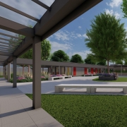 A foto é uma maquete que mostra o pátio central de uma escola, uma área ao ar livre e pavimentada com lajes de concreto claras. No centro, há uma área de grama com uma árvore grande e bancos curvos ao redor. As laterais do pátio são formadas por prédios com fachadas coloridas em tons de vermelho e amarelo. Existem bancos de madeira e estruturas de concreto para sentar. 