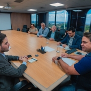 A foto mostra um grupo de várias pessoas sentadas ao redor de uma mesa de conferência em uma sala de reuniões. O vice-governador Gabriel Souza está no lado esquerdo da mesa, e o secretário nacional de Transporte Ferroviário, Leonardo Ribeiro, está no lado oposto, de frente para a câmera. Todos estão prestando atenção à discussão.