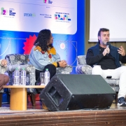 A fotografia mostra três pessoas sentadas em poltronas em um palco, participando de uma discussão em painel. Da esquerda para a direita, estão a presidente da Gramadotur, Rosa Helena Volk, que sorri e veste um blazer xadrez claro. Ao lado dela, a coordenadora institucional do Festival de Cinema de Cartagena, Gisela Perez Fonseca, usa uma jaqueta colorida e olha na direção do orador. Na direita, o diretor-presidente da Embratur, Marcelo Freixo, segura um microfone e gesticula enquanto fala. Ele está de blusa preta e calça branca.