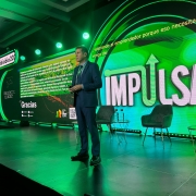 A imagem mostra um palco de evento com iluminação em tons de verde e um telão de LED ao fundo. No centro, um homem branco, vestido com um terno azul-escuro e gravata, está em pé, segurando um microfone. Ele aparenta estar discursando ou fazendo uma apresentação.

Atrás dele, o telão de LED exibe o título "IMPULSA" em letras grandes e brancas, com a palavra "bio" em verde. Ao lado direito, na mesma tela, há a frase "valorando al emprendedor porque eso necesitamos. Yo vengo del" (valorizando o empreendedor porque é disso que precisamos. Eu venho do).

Na parte esquerda do telão, há um texto em português que menciona o Governador Eduardo Leite. O texto diz: "Estamos, em nome do Governador Eduardo Leite, quero expressar mi gratidão por esta oportunidad de estar aquí e agradecer pelo trabalho que tem sido feito no Estado do Rio Grande do Sul e pela região [...] É um privilégio para nós fazermos parte do Rio Grande do Sul. E que estamos orgulhosos de viver em um estado. Uma terra [...] grande, com as pessoas que nós temos. Somos muito agradecidos de fazer parte, gerando riqueza e gerando desenvolvimento. Agradecemos ao desenvolvimento do Rio Grande do Sul." Abaixo deste texto, há a palavra "Gracias" (Obrigado) em letras grandes e brancas.

No canto superior esquerdo, há a hashtag #impulsaBio2025. Ao lado, o nome "CHILE CORTE DE LOS ANDES" (CHILE CORTE DOS ANDES) está escrito em branco.

No palco, à frente do telão, há duas cadeiras de design moderno e duas pequenas mesas de apoio, cada uma com uma garrafa de água e um copo. O chão do palco é preto e brilhante. O ambiente geral é de um evento corporativo ou de inovação.