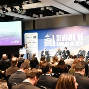 Auditório cheio, com público sentado voltado para o palco, onde ocorre um painel durante a Semana de Barragens 2025. À esquerda, uma mulher está em pé, atrás de um púlpito, realizando apresentação. Ao fundo, um telão projeta a palavra “Obrigada” e o nome de Marjorie Kauffmann, secretária estadual do Meio Ambiente e Infraestrutura. No centro do palco, cinco homens sentados participam do debate. O cenário exibe o painel azul e branco com os dizeres “Semana de Barragens 2025 – Damsweek” e a data do evento, 24 a 29 de agosto, em Porto Alegre.