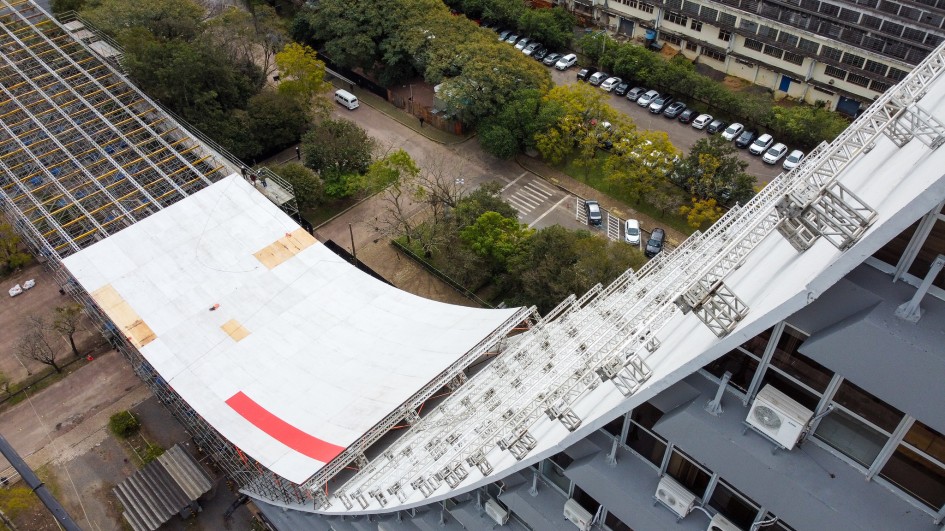 Foto tirada de cima para baixo da rampa, de cor branca, sendo montada no Caff. A curva do prédio aparece à direita, com a rampa à esquerda do quadro.