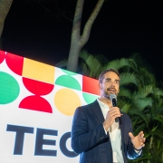 O governador Eduardo Leite está ao centro da imagem, falando ao microfone. Ao fundo, há um painel colorido (nas cores verde, vermelho e amarelo), com a identidade visual do RS Tech. 