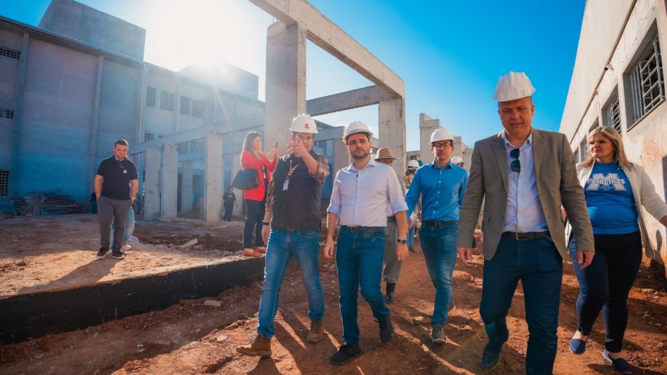 Um grupo de pessoas, com o vice-governador ao centro, caminha em meio a um canteiro de obras na escola.