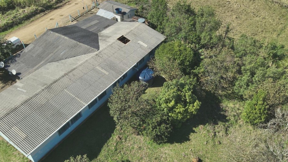 Foto aérea, feita por drone, mostra uma cisterna azul ao lado de uma escola, localizada do lado esquerdo da imagem. Ao lado direito, há diversas copas de árvores verdes.