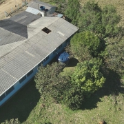 Foto aérea, feita por drone, mostra uma cisterna azul ao lado de uma escola, localizada do lado esquerdo da imagem. Ao lado direito, há diversas copas de árvores verdes. 