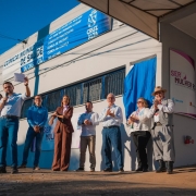 O vice-governador Gabriel Souza aparece em primeiro plano, de camiseta branca e jeans, discursando ao microfone durante a inauguração do 13º Serviço Especializado de Referência à Saúde da Mulher (SERMulher RS), em Cruz Alta. Ao lado dele, em frente ao prédio identificado como Clínica Municipal de Saúde de Cruz Alta, estão autoridades estaduais e municipais, homens e mulheres, que aplaudem e sorriem. À direita da imagem, próximo à entrada do prédio, há uma faixa do programa Ser Mulher RS e uma decoração com balões lilás. O evento ocorre em área externa, sob céu azul.
