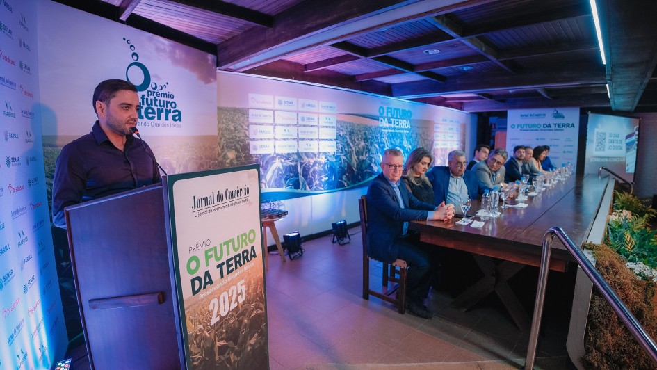 Foto de de ambiente fechado, de coloração azul, com Gabriel, à esquerda, discursando junto ao púlpito. À direita, há uma mesa com várias pessoas sentadas em fila.