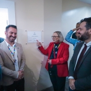 Foto mostra a secretária Arita Bergamann apontando para um placa branca na inauguração. Há outras autoridades engravatadas que sorriem.