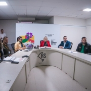 Foto em uma sala de reuniões, com três homens e três mulheres reunidos. A secretária da Saúde está posicionada ao centro. 