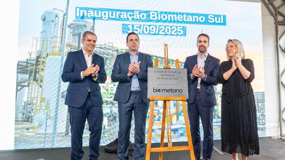 Fotografia da cerimônia de inauguração da Biometano Sul, realizada em 15 de setembro de 2025, em Minas do Leão (RS). No centro da imagem, há uma placa metálica sobre cavalete de madeira, com os dizeres “Unidade de Geração de Biometano em Minas do Leão – inaugurada em 15 de setembro de 2025 – Biometano Sul”. Ao redor da placa, quatro pessoas em trajes formais posam para a foto: três homens de terno e uma mulher de vestido preto, todos sorrindo e aplaudindo. Ao fundo, um telão exibe o título “Inauguração Biometano Sul – 15/09/2025”.