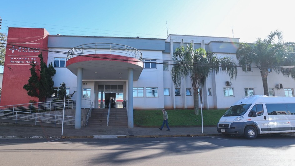 Foto da fachada do Hospital S&atilde;o Vicente de Paulo. Ao lado esquerdo, em uma torre vermelha, &eacute; poss&iacute;vel ler o nome da institui&ccedil;&atilde;o. O hospital est&aacute; pintado em tons de cinza e branco. H&aacute; duas &aacute;rvores na frente da institui&ccedil;&atilde;o. 