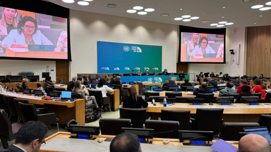 A imagem mostra uma sessão em andamento nas Nações Unidas (ONU), possivelmente durante uma cúpula climática, como indicado pelo painel azul ao fundo com o texto "Climate Ambition Summit 2023". A sala está cheia de delegados e participantes sentados em mesas organizadas em formato semicircular, típicas de sessões da ONU.
Em destaque, dois telões mostram uma mulher discursando com o microfone ligado e um cronômetro marcando o tempo da fala (0:56). A plaquinha à sua frente indica "ICLEI", uma organização global voltada para sustentabilidade local. A plateia acompanha atentamente, com notebooks e documentos abertos, evidenciando o caráter técnico e diplomático do evento. A atmosfera é formal e voltada à discussão de políticas internacionais relacionadas ao clima.