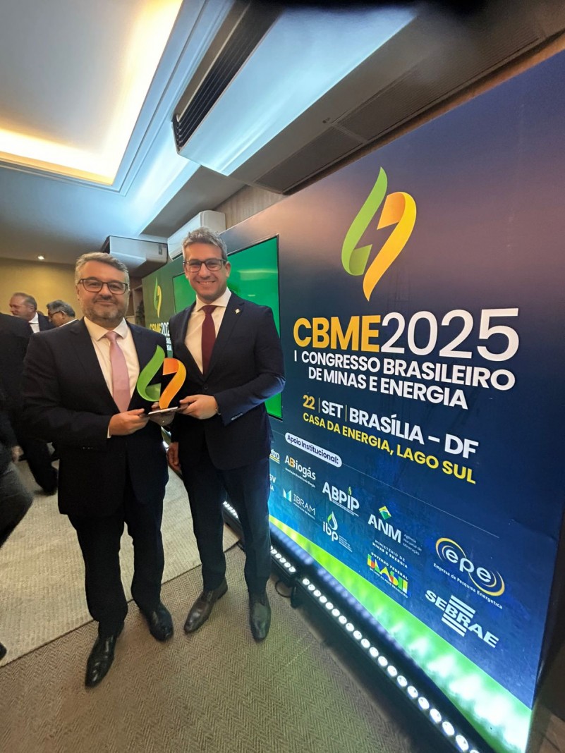 A imagem mostra dois homens de terno escuro posando para a foto em um evento. Ambos estão sorrindo e segurando um troféu com o logotipo do evento. Ao fundo, há um grande painel com o texto:
"CBME 2025 – I Congresso Brasileiro de Minas e Energia
22 SET | BRASÍLIA – DF
CASA DA ENERGIA, LAGO SUL"
Abaixo do título principal, há diversos logotipos de instituições apoiadoras do evento, como EPE, SEBRAE, ANM, ABPIP, IBRAM, IDP, ABiogás, entre outros.
O ambiente parece ser uma sala de conferências ou auditório, com iluminação clara e pessoas ao fundo interagindo.