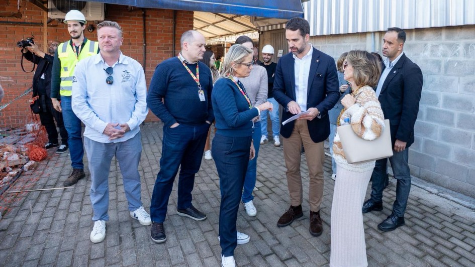 O governador Eduardo Leite aparece em visita às obras da Escola La Salle, em Campo Bom. Ele conversa com técnicos e gestores, observando documentos apresentados. O grupo está em área externa, próxima a um prédio de tijolos à vista e estruturas metálicas, onde trabalhadores com capacetes acompanham a vistoria.