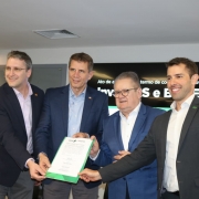 Foto mostra o secretário Ernani Polo, o diretor-presidente do BRDE, Ranolfo Vieiras Júnior, (ambos de terno azul, ao centro), o presidente da Invest RS, Rafael Prikladnicki e o diretor de Planejamento do BRDE, Leonardo Busatto. Eles seguram juntos um documento e posam para foto.