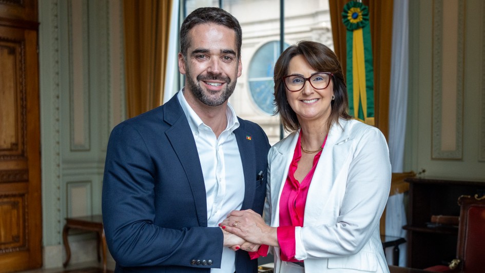 Governador Eduardo Leite e a secretária da Mulher, Fábia Richter. Eles se cumprimentam de mãos juntas e olham sorridentes para a câmera.
