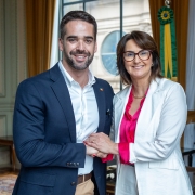 Governador Eduardo Leite e a secretária da Mulher, Fábia Richter. Eles se cumprimentam de mãos juntas e olham sorridentes para a câmera.