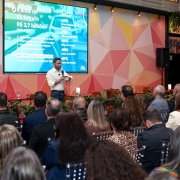 A imagem apresenta um evento, com foco na plateia e no vice-governador, que é o palestrante. Ao fundo, uma tela exibe informações sobre “6 anos do RS Seguro” e dados financeiros, como “R$ 3,7 bilhões”, além de percentuais relacionados a indicadores de segurança.