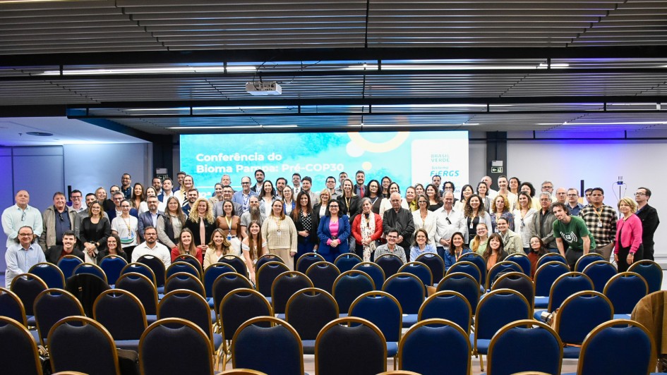 A imagem mostra uma foto coletiva com dezenas de pessoas reunidas no palco e à frente dele, posando para registro oficial. Ao fundo, a tela exibe o texto “Conferência do Bioma Pampa – Pré-COP30” e o logotipo do Fórum Gaúcho de Mudanças Climáticas (FGMC).