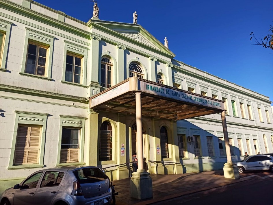 Fachada da Irmandade da Santa Casa de Caridade de São Gabriel sob luz solar. O prédio histórico tem paredes em tom verde-claro e janelas com molduras amarelas.