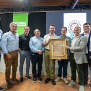 Um grupo de homens está reunido em pé, posando para a foto. Ao centro, segurando um quadro com moldura dourada, está o governador.