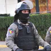 Três policiais usam câmeras corporais. Eles usam máscaras e capacetes. 