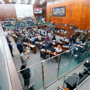 Imagem mostra uma votação na Assembleia Legislativa, com diversas pessoas sentadas ou em pé em suas mesas. Ao fundo, há um telão com a votação. 