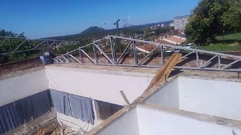 A imagem apresenta uma construção sem telhado, com paredes brancas e vigas metálicas parcialmente instaladas sobre a estrutura.