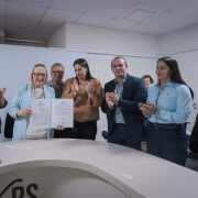 Secretaria Arita Bergmann com documento na mão enquanto outras pessoas na foto batem palmas.