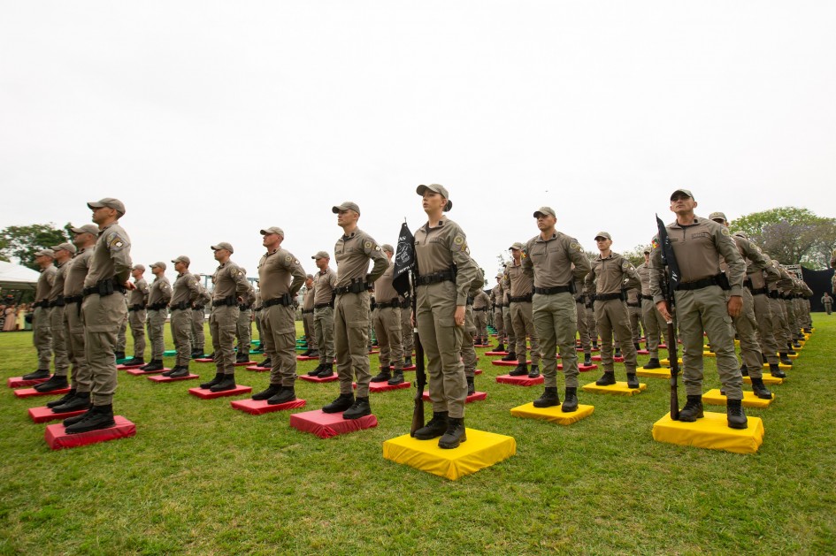 Formandos da Brigada Militar estão perfilados em posição de sentido, organizados sobre colchonetes coloridos, durante o momento solene da formatura.