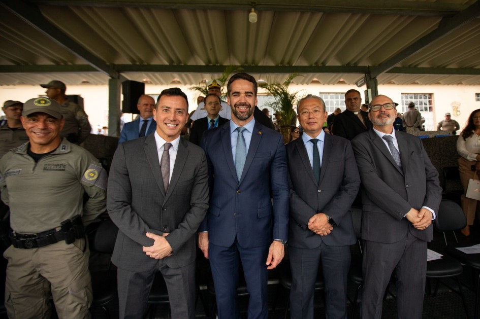 O governador Eduardo Leite aparece ao centro, sorrindo, ao lado de autoridades civis e militares durante a cerimônia. Entre eles o secretário da Segurança Pública, Sandro Caron, e o substituto que irá ocupar o cargo, coronel Ikeda.
Todos posam para foto na área de honra, sob o pavilhão da Brigada Militar.