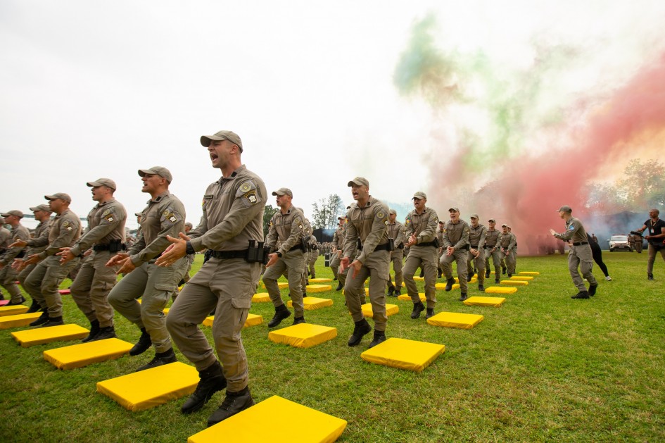 Soldados da Brigada Militar realizam apresentação coreografada sobre colchonetes coloridos, com fumaça nas cores verde, vermelha e amarela ao fundo, simbolizando o Rio Grande do Sul.