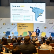 O governador Eduardo Leite apresenta o painel durante evento em São Paulo. Ele fala diante de um auditório cheio, com slide projetado ao fundo mostrando mapa do Brasil e indicadores de economia e qualidade de vida do Estado.