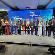 Grupo de 17 pessoas posa no palco segurando troféus do Prêmio Pesquisador Gaúcho 2025. Homens e mulheres estão alinhados diante de um grande painel azul com o tema “Ciência para reconstrução e resiliência”. A cena transmite um clima de celebração e reconhecimento à pesquisa científica.