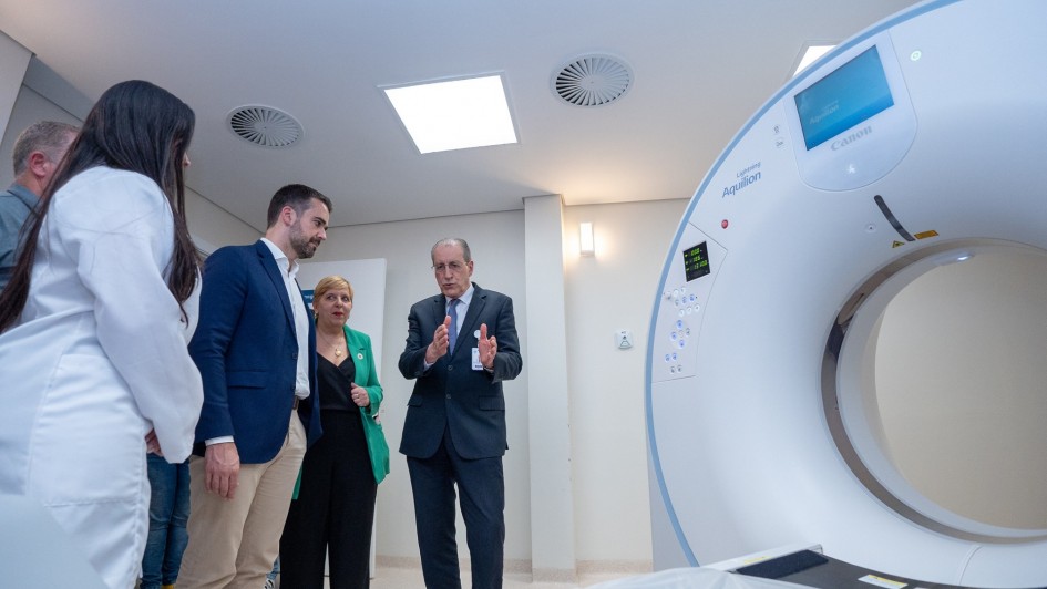 O governador Eduardo Leite (de terno azul e camisa branca) observa a demonstração do funcionamento de um tomógrafo em hospital, ao lado de profissionais da saúde e autoridades. Um homem de terno escuro explica o equipamento, enquanto uma mulher de blazer verde acompanha atentamente.