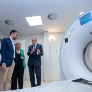 O governador Eduardo Leite (de terno azul e camisa branca) observa a demonstração do funcionamento de um tomógrafo em hospital, ao lado de profissionais da saúde e autoridades. Um homem de terno escuro explica o equipamento, enquanto uma mulher de blazer verde acompanha atentamente.