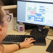 Imagem em plano fechado exibe uma servidora da Secretaria de Obras Públicas, de perfil, visualizando projeto de engenharia na tela em seu computador de trabalho.