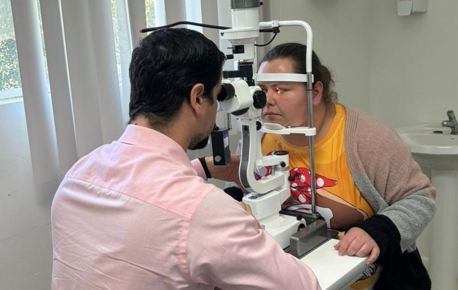 Mulher passando por exame ocular com aparelho de luz, enquanto profissional observa de perto. Esteja em consultório médico.