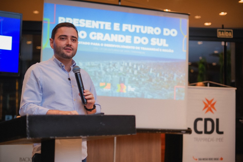 O vice-governador Gabriel Souza aparece em pé, segurando um microfone e falando diante de uma tela de projeção. O slide ao fundo exibe o título “Presente e Futuro do Rio Grande do Sul” e o logotipo da CDL Tramandaí.