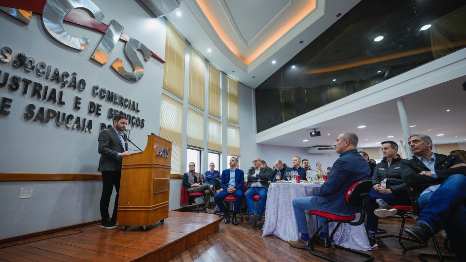 O vice-governador Gabriel Souza aparece em pé, falando ao microfone em um púlpito com o logotipo “ACIS”. À frente dele, há várias pessoas sentadas em cadeiras vermelhas, observando a apresentação.