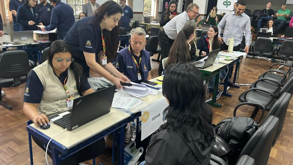 Foto mostra sala montada para o atendimento, tendo trabalhadores e moradores da cidade de Bagé trocando informações em mesas com computadores