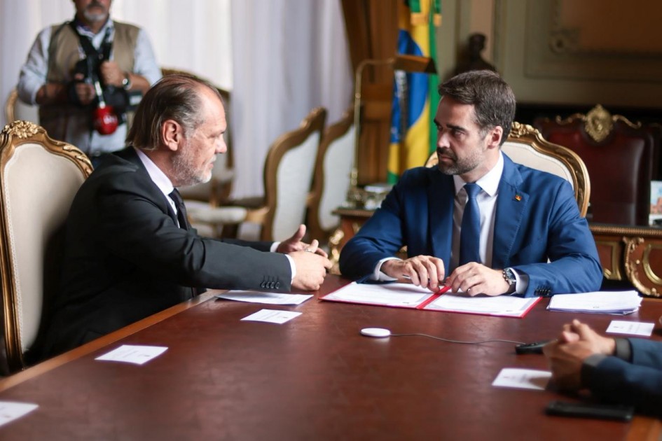 O governador Eduardo Leite, à direita, conversa com o presidente do Tribunal de Justiça do RS, desembargador Alberto Delgado Neto, à esquerda. Ambos estão sentados em mesa de reunião no Palácio Piratini, com o documento da permuta à frente.